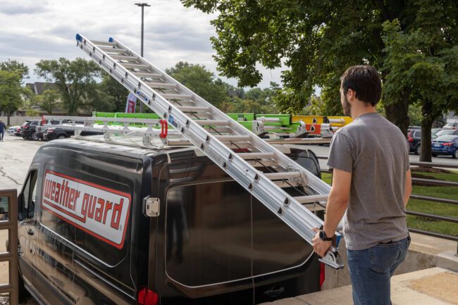 View of man loading ladder onto a Weather Guard Safari ladder rack installed on a full-size van.